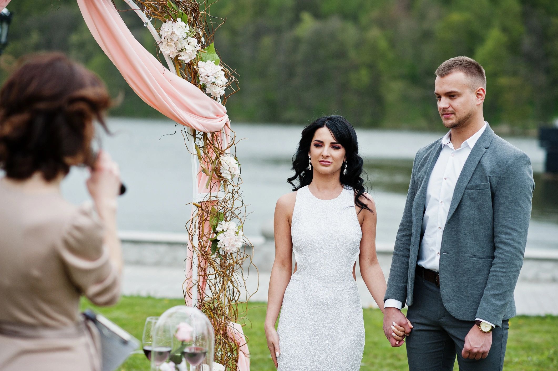 Young fashionable lovely couple with speech master of wedding ceremony against decor arch on wedding anniversary and marriage proposal.